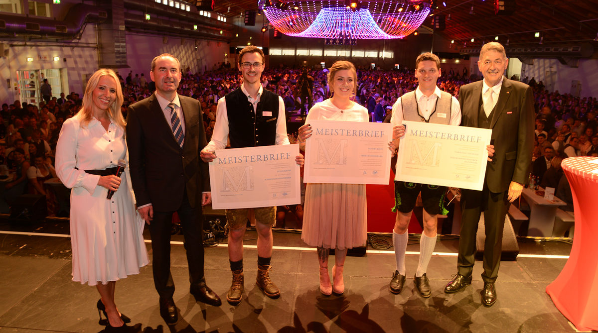 Bayerns Wirtschaftsminister Hubert Aiwanger (2. v. li.), HWK-Präsident Dr. Georg Haber (1. v. re.) und Moderatorin Katja Wunderlich (1. v. li.) überreichten den drei Absolventen (v. li. n. re.) Felix Kroiß, Sandra Kiefl und Christian Thurner auf der Bühne die Meisterbriefe. Bayerns Wirtschaftsminister Hubert Aiwanger (2. v. li.), HWK-Präsident Dr. Georg Haber (1. v. re.) und Moderatorin Katja Wunderlich (1. v. li.) überreichten den drei Absolventen (v. li. n. re.) Felix Kroiß, Sandra Kiefl und Christian Thurner auf der Bühne die Meisterbriefe.