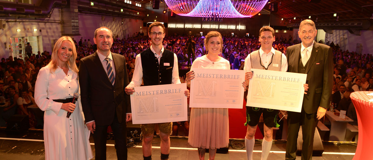 Bayerns Wirtschaftsminister Hubert Aiwanger (2. v. li.), HWK-Präsident Dr. Georg Haber (1. v. re.) und Moderatorin Katja Wunderlich (1. v. li.) überreichten den drei Absolventen (v. li. n. re.) Felix Kroiß, Sandra Kiefl und Christian Thurner auf der Bühne die Meisterbriefe. Bayerns Wirtschaftsminister Hubert Aiwanger (2. v. li.), HWK-Präsident Dr. Georg Haber (1. v. re.) und Moderatorin Katja Wunderlich (1. v. li.) überreichten den drei Absolventen (v. li. n. re.) Felix Kroiß, Sandra Kiefl und Christian Thurner auf der Bühne die Meisterbriefe.
