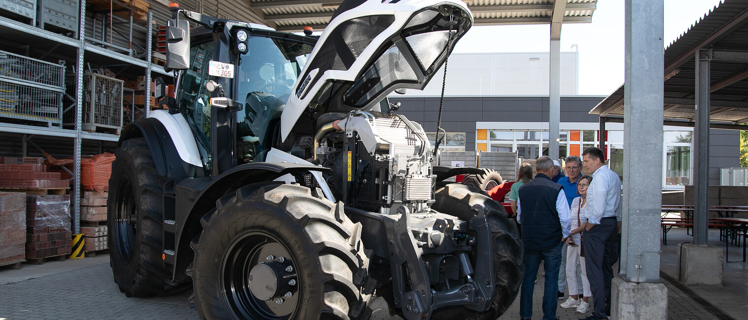 Die Motorhaube des Traktors der Innung für Land- & Baumaschinentechnik wurde geöffnet, einige Menschen stehen interessiert daneben. 