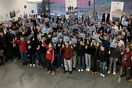 Die 120 Schülerinnen und Schüler in der Aula der Realschule. Alle halten Handwerks-Fahnen in die Luft.