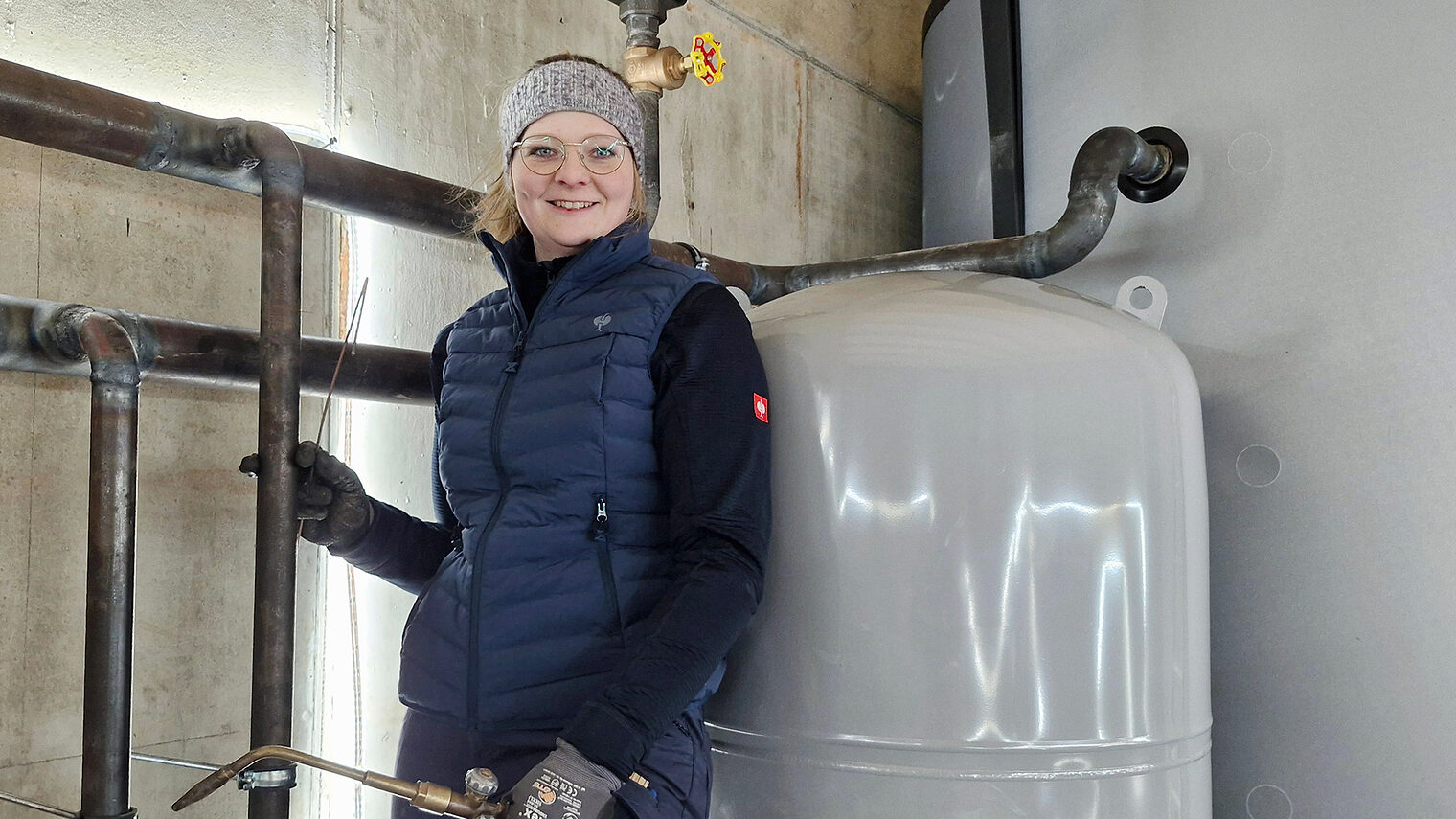 Installateur- und Heizungsbaumeisterin Stefanie Brehm posiert vor einem großen Heizkessel.