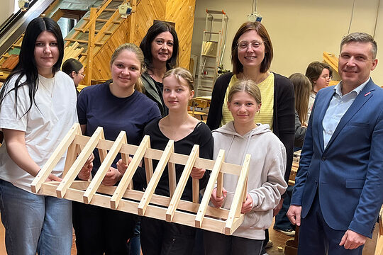 Schülerinnen der Sophie-Scholl-Realschule halten einen selbstgezimmerten, kleinen Dachstuhl in die Kamera. 