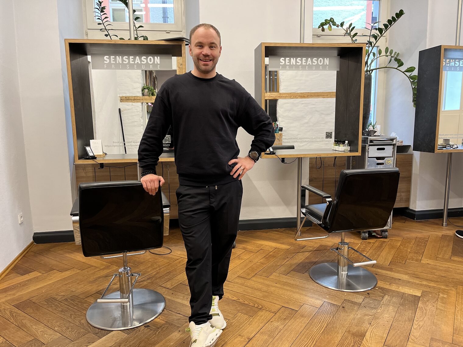 Friseurmeister Eusemann Thomas steht stolz in seinem Friseurladen und lächelt in die Kamera.