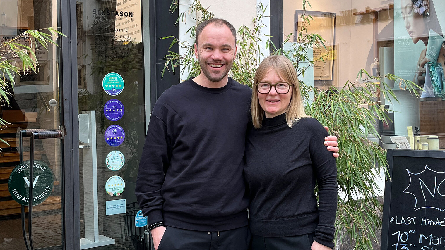 Thomas und Jeanette Eusemann stehen Arm in Arm vor ihrem eigenen Friseursalon, den sie sich gemeinsam aufgebaut haben.