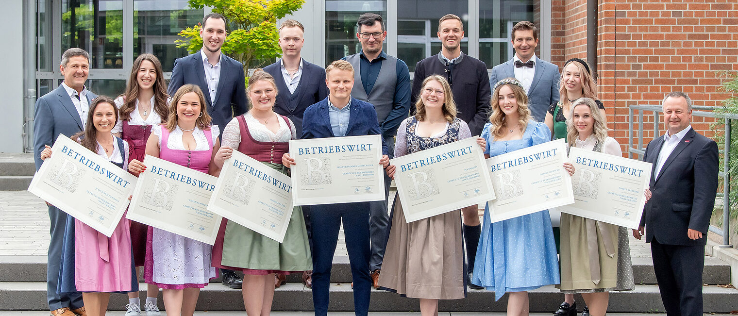 Die Betriebswirte halten fröhlich ihre Zeugnisse in die Kamera. Die Ehrengäste freuen sich mit ihnen. 