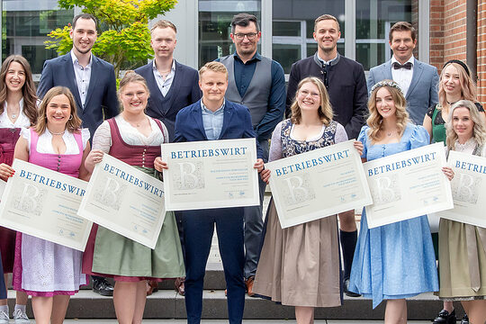 Die Betriebswirte halten fröhlich ihre Zeugnisse in die Kamera. Die Ehrengäste freuen sich mit ihnen. 
