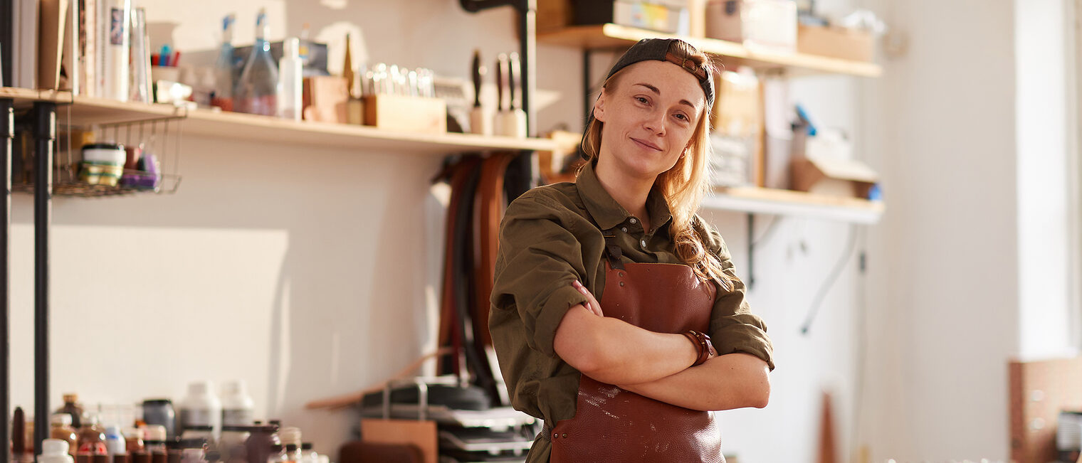 Positivtrend: Immer mehr Frauen gründen im Handwerk. Eine selbstbewusste Frau steht in ihrer Werkstatt, überkreuzt die Arme und schaut in die Kamera.