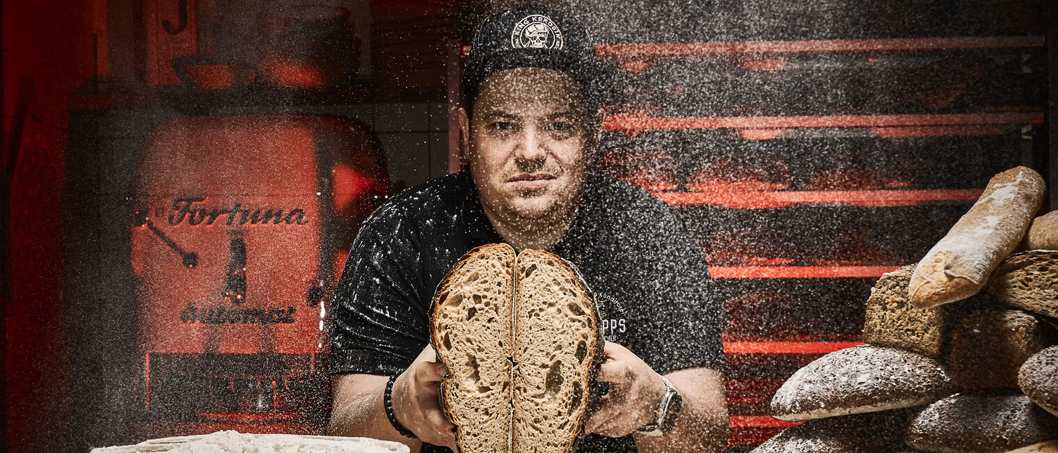 Christian Philipps hat sich mit seinem 360 Grad Laib bundesweit einen Namen gemacht. In einer rustikalen Bäckerei-Kulisse präsentiert Konditormeister Christian Philipps ein aufgeschnittenes Brot, während Mehlstaub in der Luft schwebt.