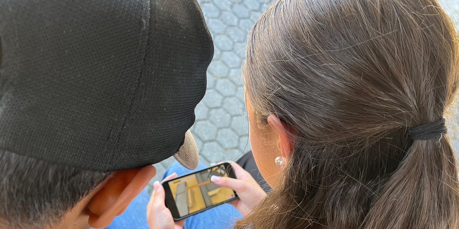 Zwei Jugendliche spielen das virtuelle Praktikum auf einem Smartphone. 