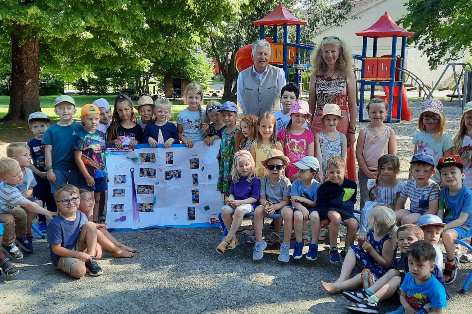 Eine Kindergartengruppe des Kindergartens Irlbach steht mit einer Erzieherin und HWK-Vizepräsident Hans Kastl im Garten vor einem Kletterturm und halten ein Plakat hoch.