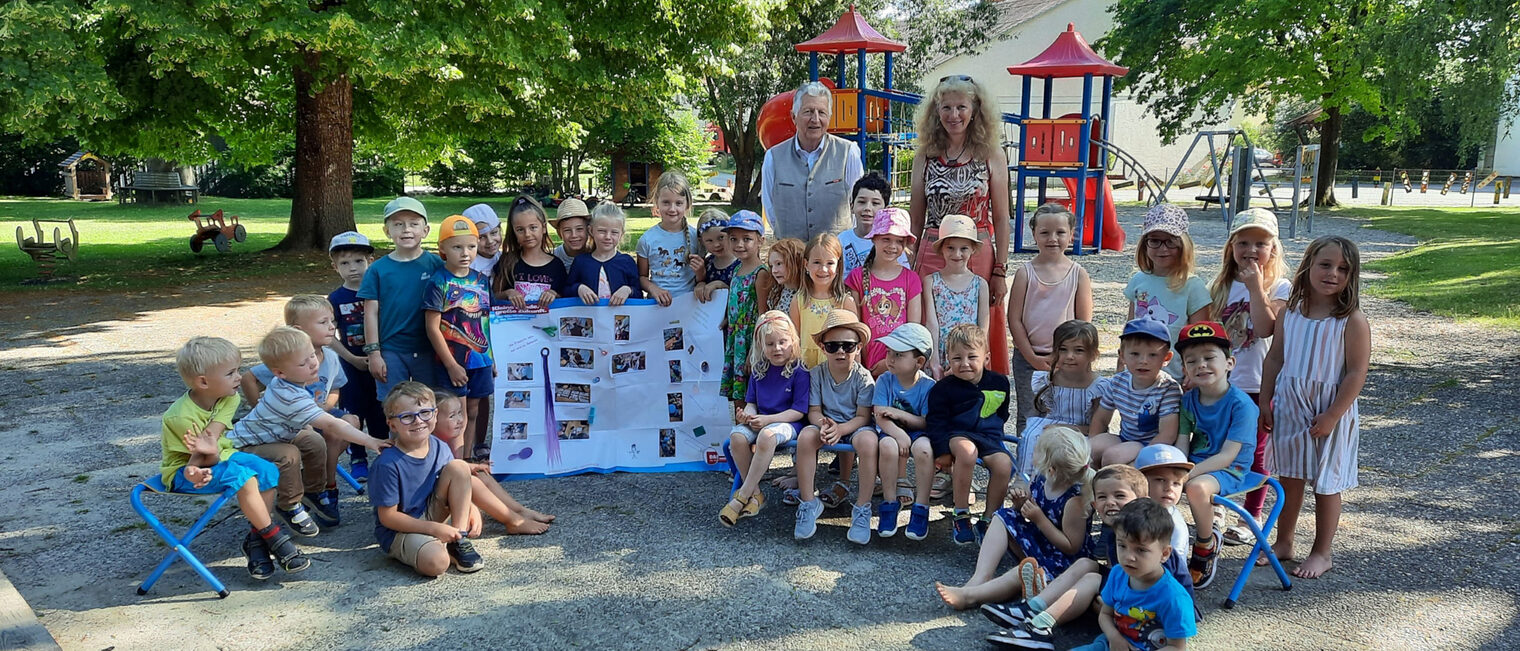 Eine Kindergartengruppe des Kindergartens Irlbach steht mit einer Erzieherin und HWK-Vizepräsident Hans Kastl im Garten vor einem Kletterturm und halten ein Plakat hoch.