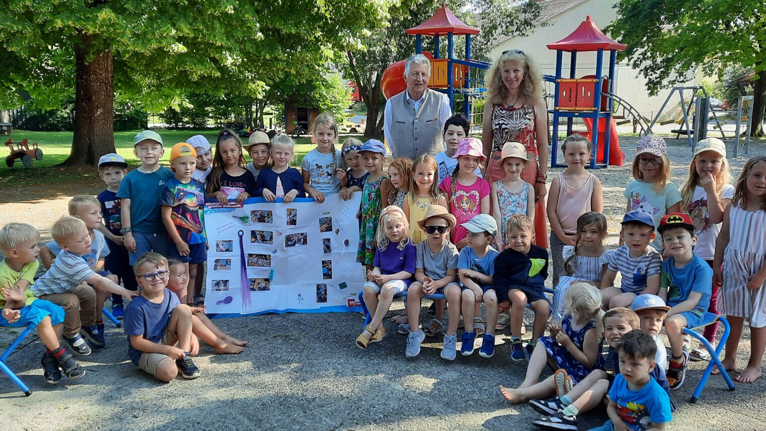Eine Kindergartengruppe des Kindergartens Irlbach steht mit einer Erzieherin und HWK-Vizepräsident Hans Kastl im Garten vor einem Kletterturm und halten ein Plakat hoch.