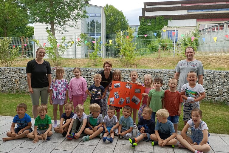 Die Kindergartenkinder mit zwei Erwachsenen und der HWK-Vizepräsidentin Claudia Geiselhöringer halten ein orangefarbenes Plakat vor einem Gebäude.