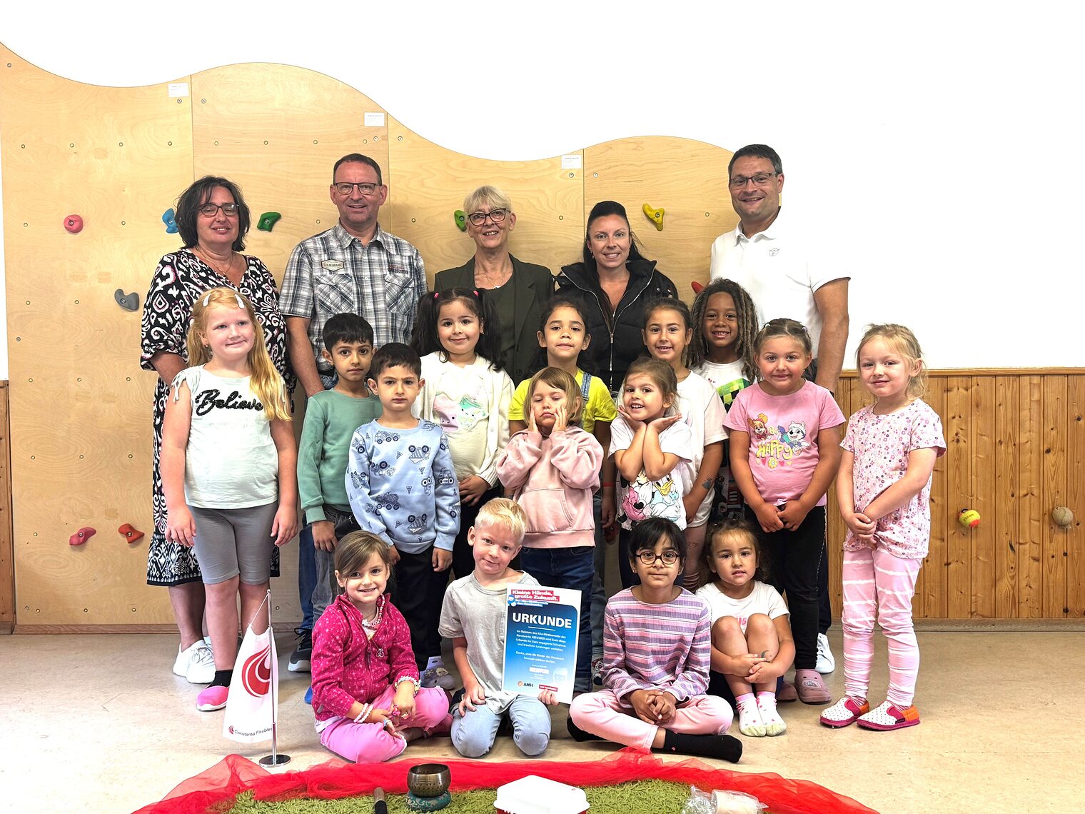 Die Kindergartenkinder, Erwachsene und HWK-Geschäftsführer Alexander Stahl posieren in einem Kindergartenraum. Ein Kind hält eine Urkunde.