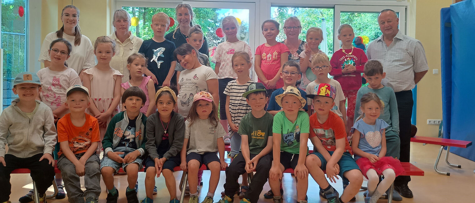 Die Kindergartengruppe, Erwachsene und HWK-Vizepräsident Christian Läpple stehen und sitzen in einem Raum mit großen Fenstern.