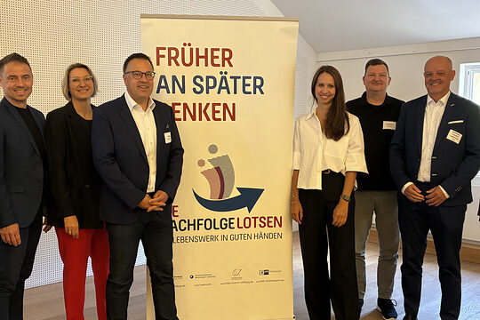 Die Organisatoren der Nachfolgelotsen freuen sich über eine gelungene Veranstaltung. Sie stehen vor dem Banner "Früher an später denken."