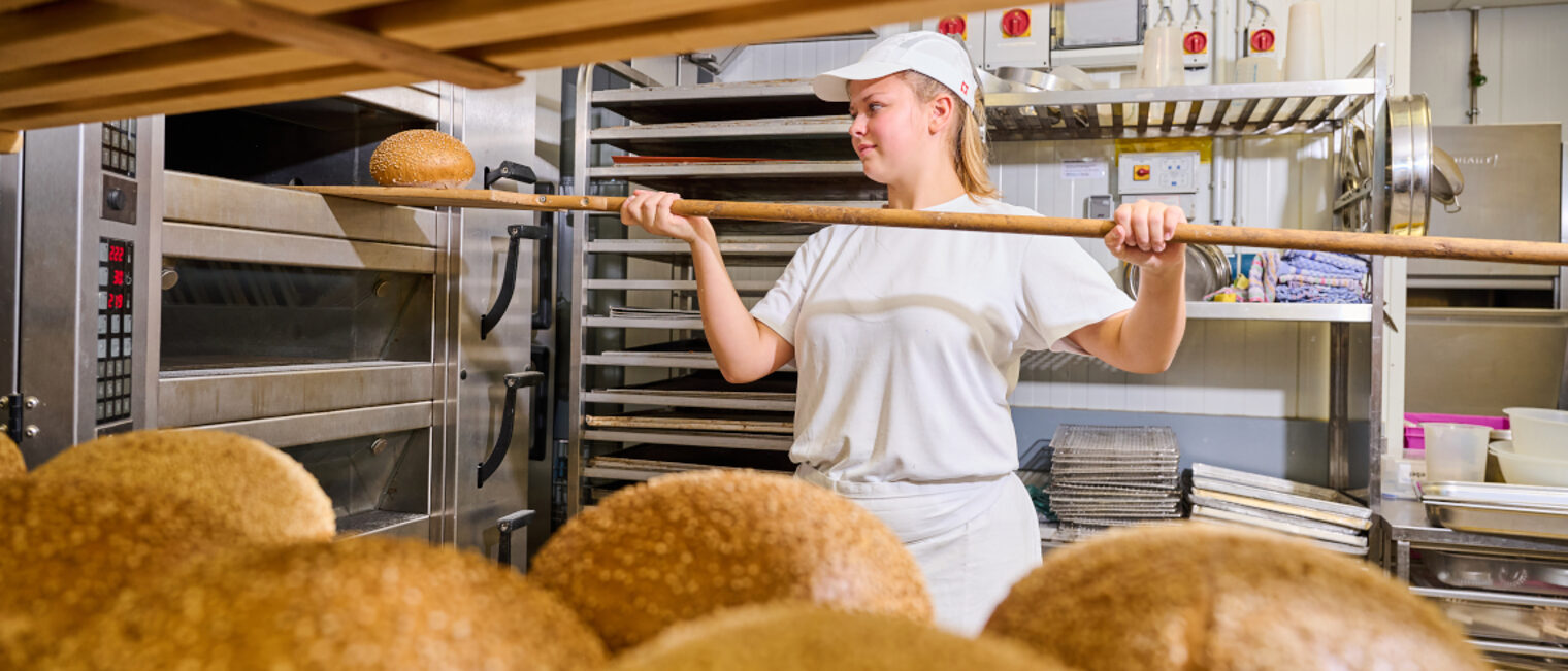 Eine Auszubildende holt ein Laib Brot aus dem Ofen. Eine Auszubildende holt ein Laib Brot aus dem Ofen.