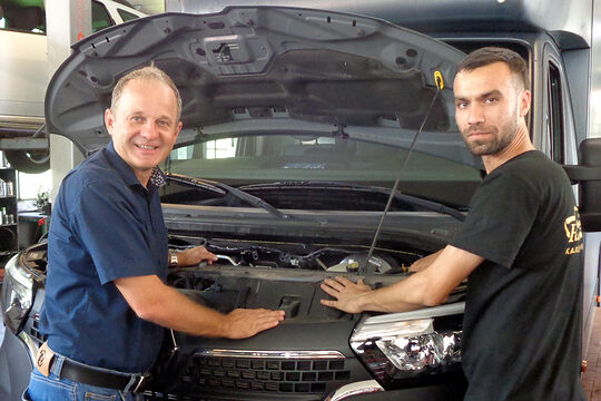 Omid Vahdani mit seinem Lehrmeister Wolfgang Feldmeier in dessen Werkstatt, sie arbeiten an einem Auto. 