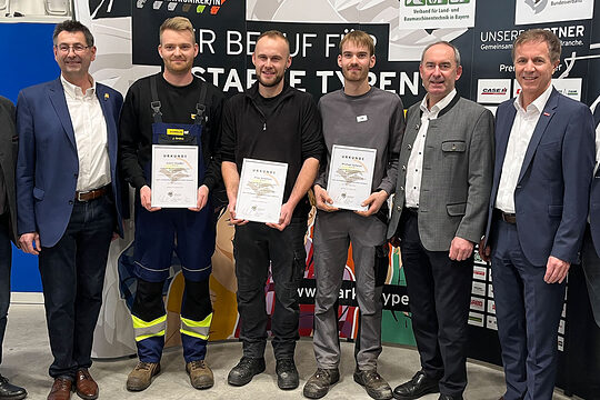 Die drei Bundessieger halten Stolz ihre Urkunden in die Kamera. Auf dem Foto sind sie mit Ehrengästen und Veranstaltern zu sehen.