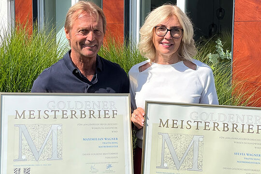 Das Ehepaar Sylvia und Maximilian Wagner lernten sich in der Meisterschule kennen. Sie halten ihre Goldenen Meisterbriefe in die Kamera. 