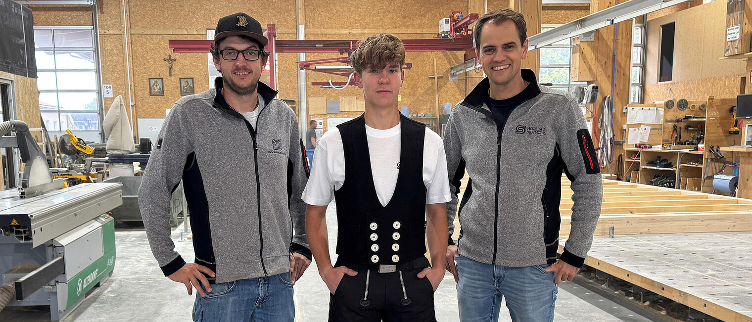 Mathias Schmid steht mittig. Er startet nächstes Jahr seine Ausbildung als Zimmerer. Geschäftsführer und Ausbildungsleiter stehen stolz neben ihm. 