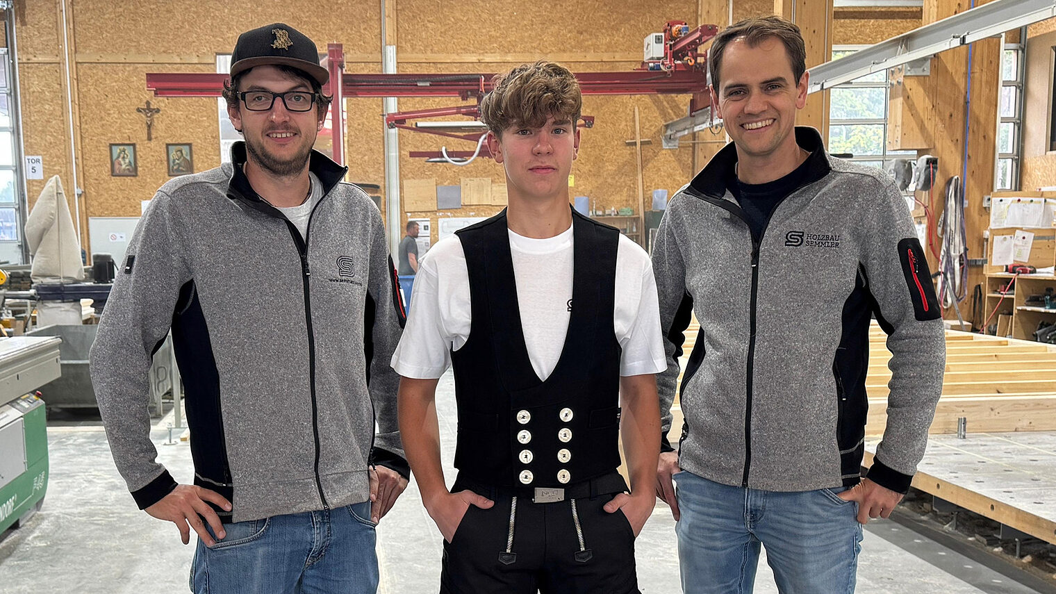 Mathias Schmid steht mittig in Zimmererkluft, daneben der stolze Geschäftsführer Max Semmler und der Ausbildungsleiter Josef Ferstl.