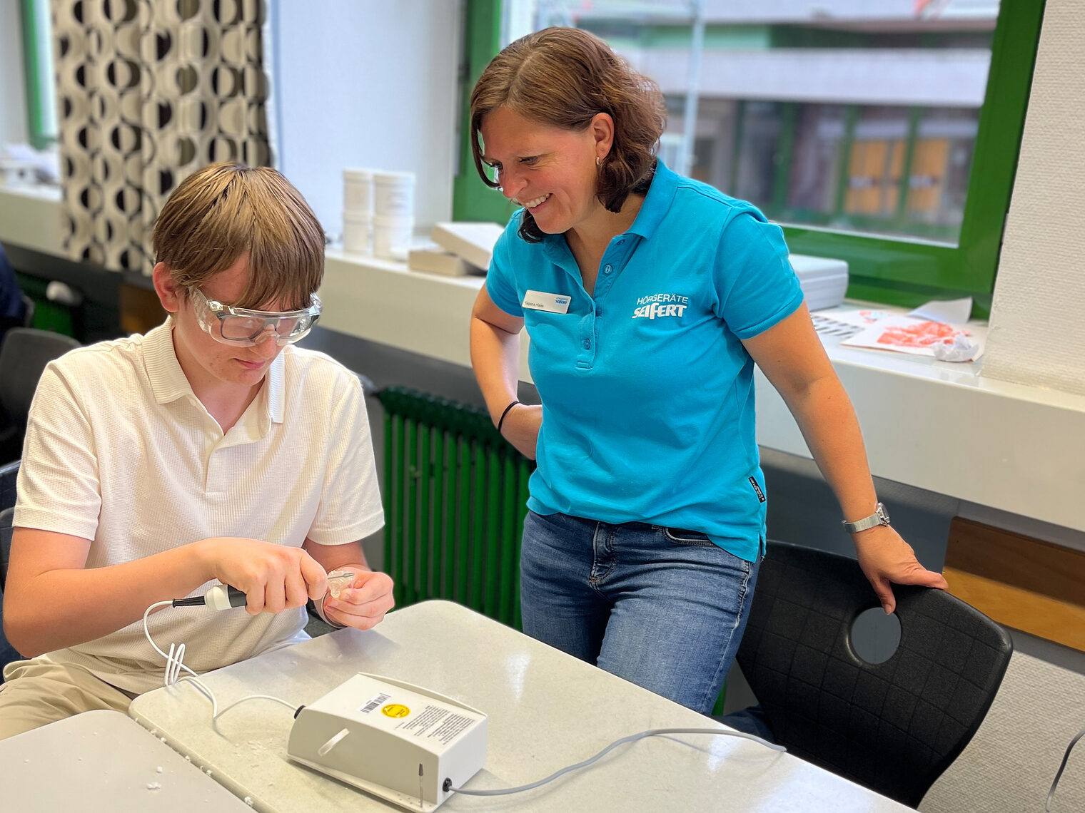 Ein Schüler misst an einem Messgerät. Die Ausbilderin schaut zu und prüft nach. 