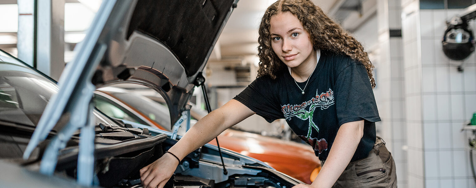 Eine Auszubildende als Kfz-Mechanikerin schraubt an einem Auto.