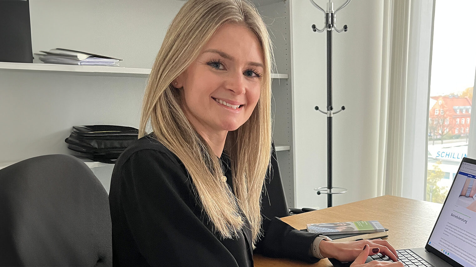 Corinna Dobmeier unterstützt die Betriebsberatung. Sie sitzt in ihrem Büro vor dem Laptop und lächelt in die Kamera.
