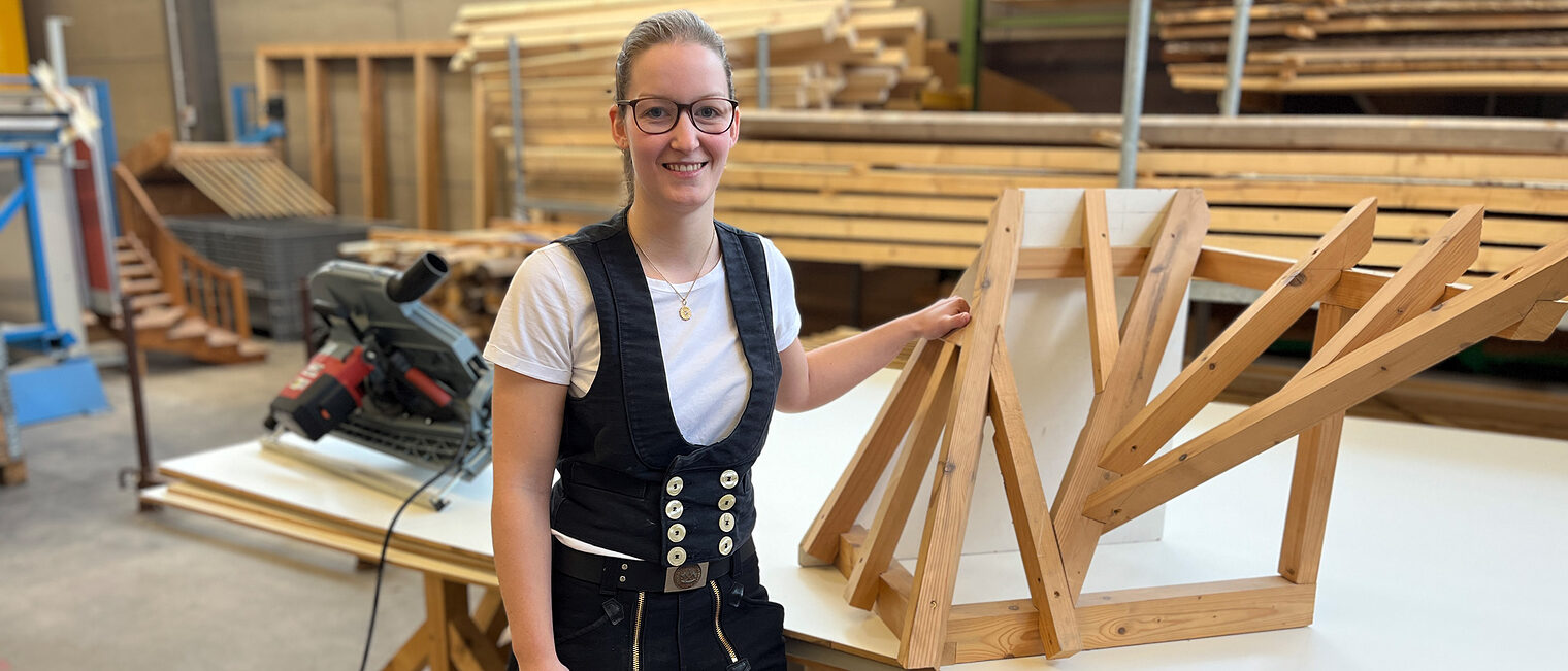 Kerstin Rei steht in der Zimmererhalle vor ihrem Meisterstück. Sie trägt stolz ihre Zimmermannskluft. 