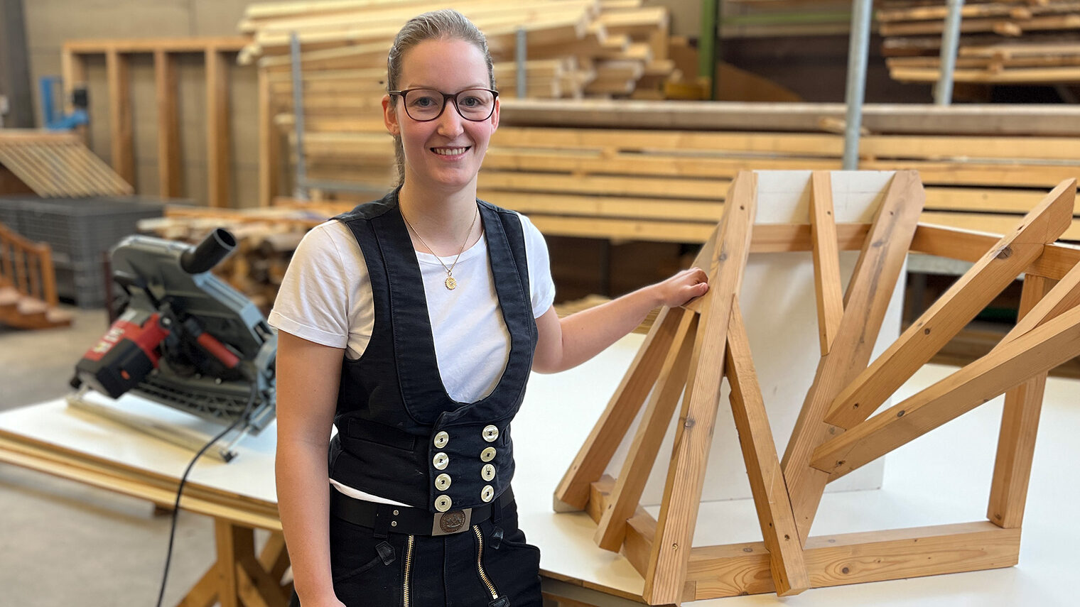 Kerstin Rei steht in der Zimmererhalle vor ihrem Meisterstück. Sie trägt stolz ihre Zimmermannskluft. 