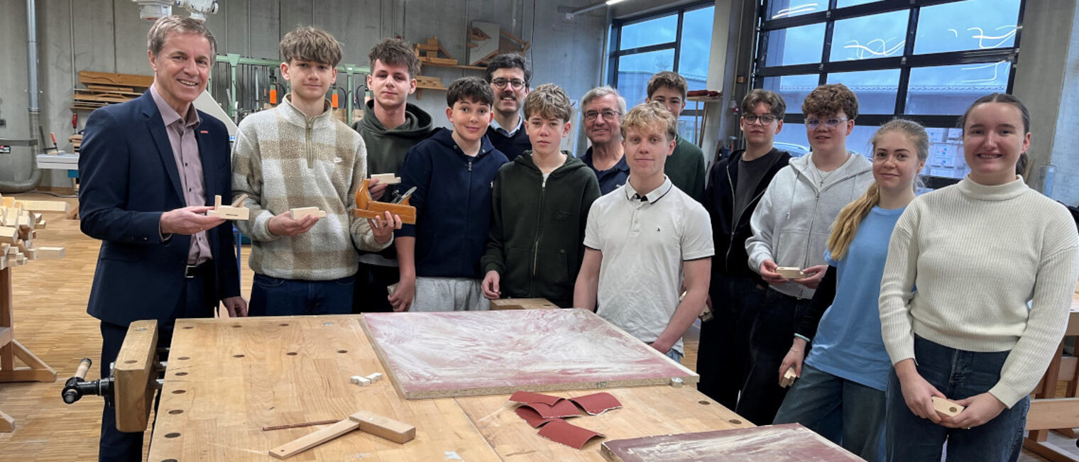 Die Schülerinnen und Schüler des Maristengymnasiums Fürstenzell stehen mit HWK-Vertetern an einer Werkbank in der Bauhalle.