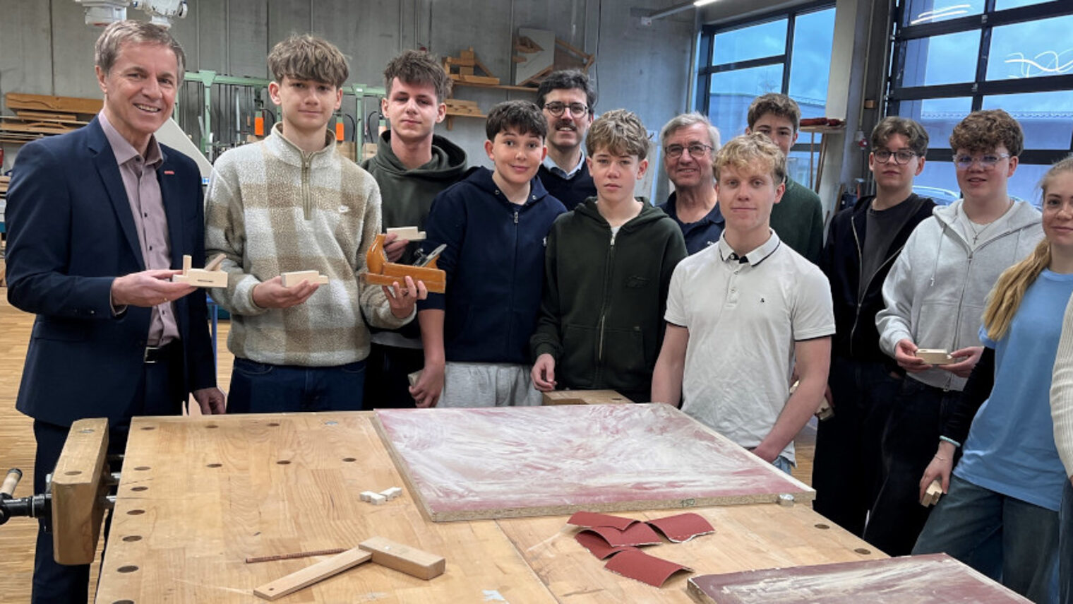 Die Schülerinnen und Schüler des Maristengymnasiums Fürstenzell stehen mit HWK-Vertetern an einer Werkbank in der Bauhalle.
