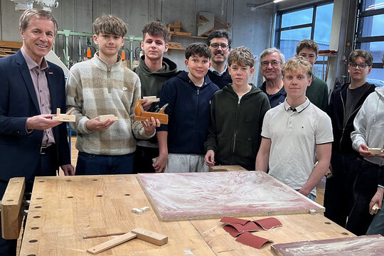 Die Schülerinnen und Schüler des Maristengymnasiums Fürstenzell stehen mit HWK-Vertetern an einer Werkbank in der Bauhalle.