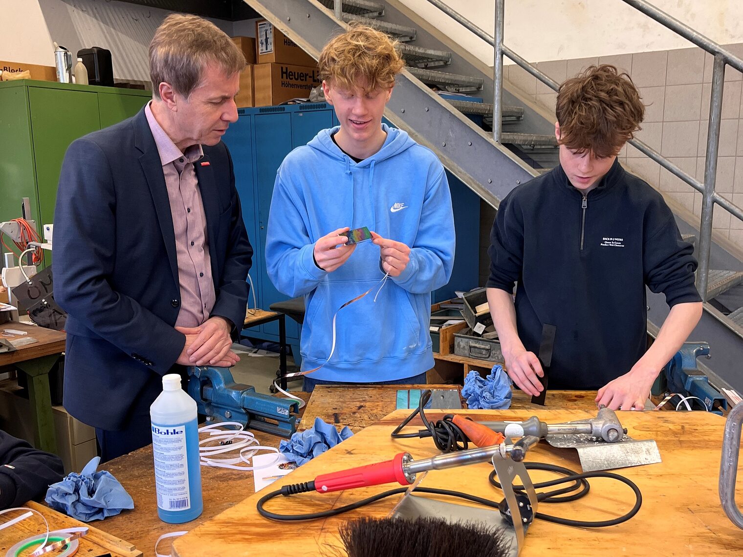 Zwei Schüler stehen mit stv. HWK-Hauptgeschäftsführer Hans Schmidt an einer Werkbank und lernen das Glaserhandwerk kennen.