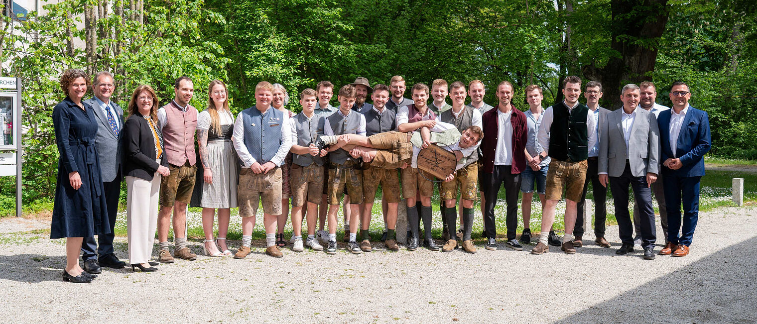 Die erfolgreichen Kursteilnehmer mit den Ehrengästen stellten sich zum Gruppenfoto auf. Mittig hält ein Absolvent eine Uhr in die Höhe.
