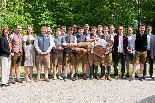 Die erfolgreichen Kursteilnehmer mit den Ehrengästen stellten sich zum Gruppenfoto auf. Mittig hält ein Absolvent eine Uhr in die Höhe.