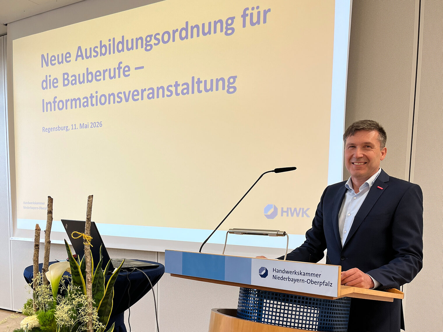Wolfgang Reif, Bereichsleiter Berufsbildung, steht vor dem Rednerpult bei der Veranstaltung. Im Hintergrund läuft die Präsentation ab.