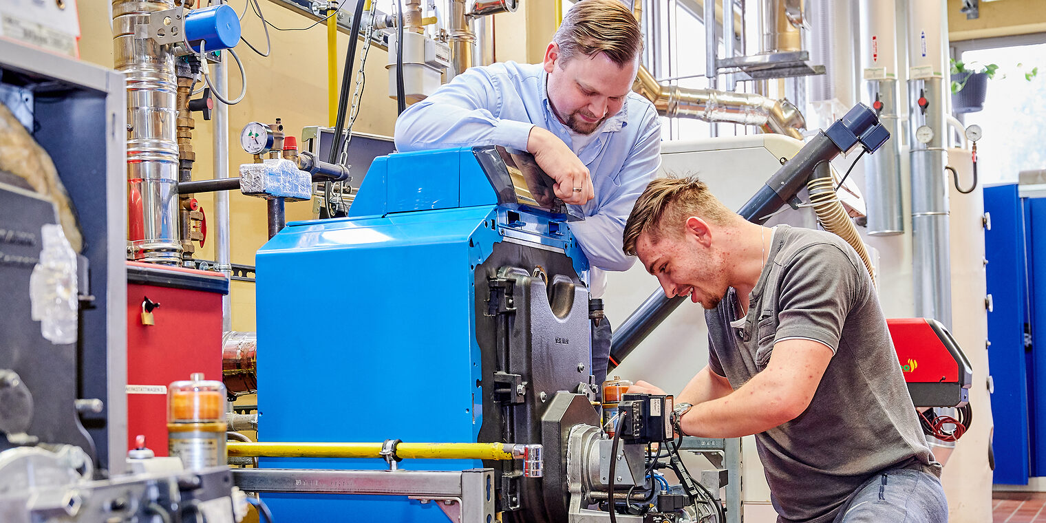Im Bildungszentrum arbeitet ein Handwerker an einer Pumpe. Der Ausbilder blickt ihm über die Schulter.