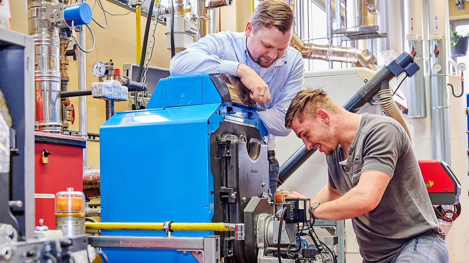 Im Bildungszentrum arbeitet ein Handwerker an einer Pumpe. Der Ausbilder blickt ihm über die Schulter.