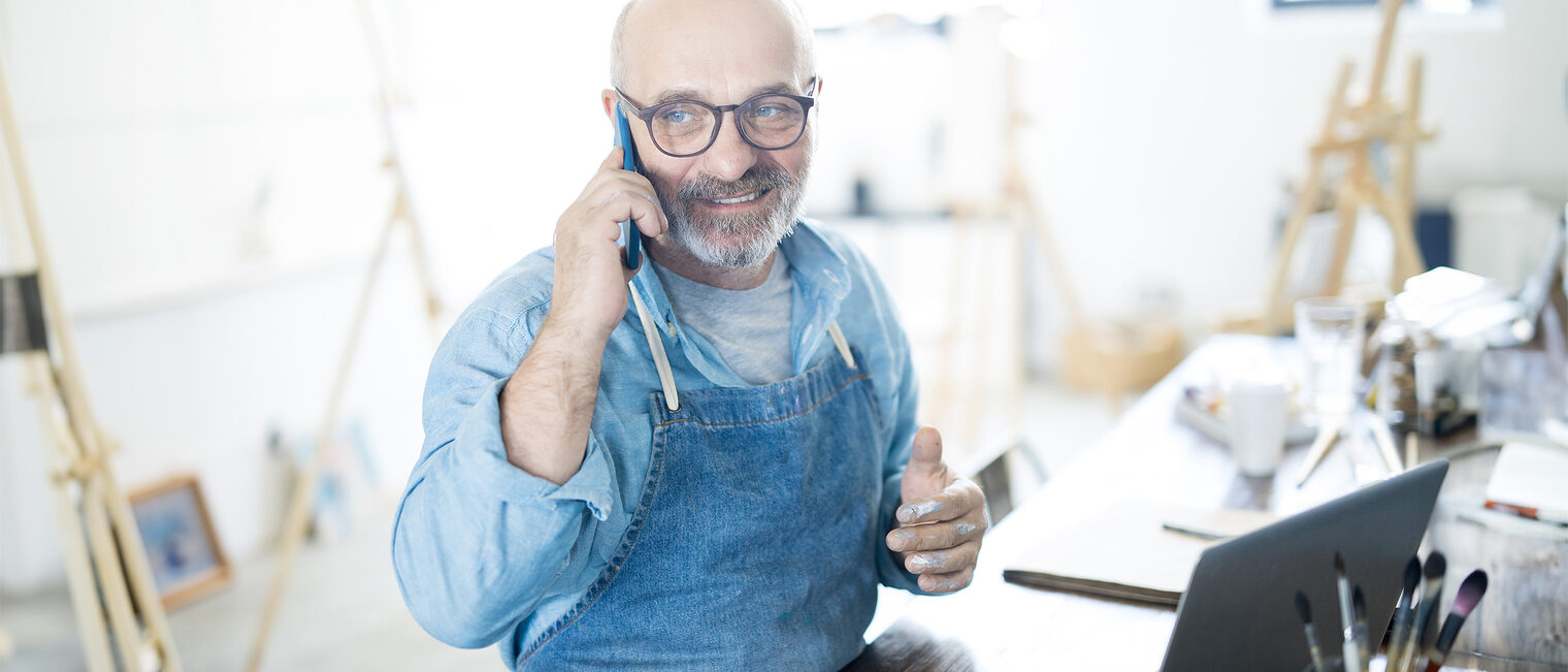 Ein Handwerker telefoniert im Büro und erledigt Arbeiten am Laptop.
